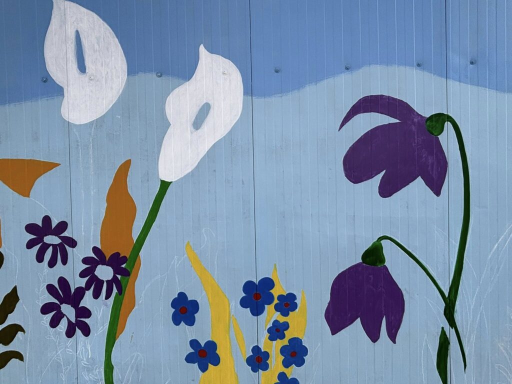 Dettaglio di un murale floreale con calle bianche, fiori viola e piccoli fiori blu dipinti su fondo azzurro.
