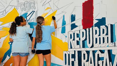 Due ragazze dipingono il murale di comunità dedicato a sport e inclusione negli spazi della Repubblica dei Ragazzi a Civitavecchia.