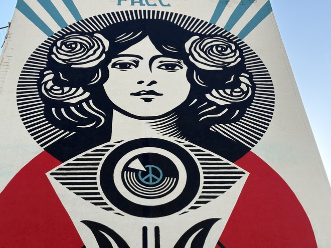 Murale monumentale con figura femminile e scritta Pace su una facciata laterale di un palazzo, visto nel contesto urbano del quartiere.